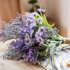 a bouquet of purple flowers sitting on top of a wooden table next to a plate