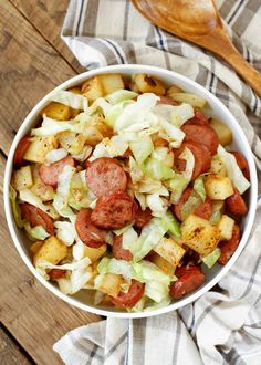 a white bowl filled with cabbage and sausage next to a wooden spoon on top of a table