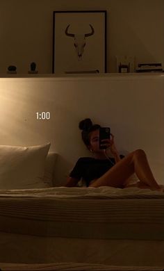 a woman sitting on top of a bed holding a cell phone in her hand and looking at the screen