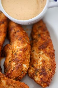 some fried chicken sticks are on a plate with dipping sauce in the bowl next to it