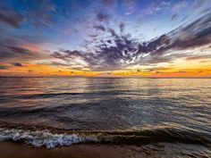 the sun is setting over the ocean with clouds in the sky and waves on the beach