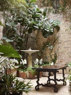 an outdoor patio with potted plants and a fountain in the center, surrounded by brick walls