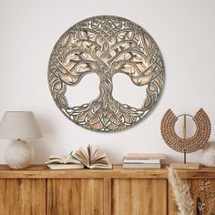 a wooden table topped with a book next to a lamp and a tree wall hanging on the wall