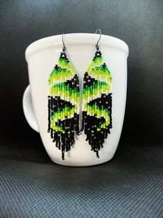 green and black beaded earrings sitting on top of a white cup with grey background