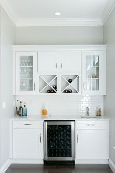 a kitchen with white cabinets and wine bottles on the counter top, in front of an oven