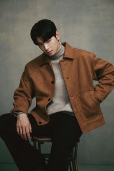 a man sitting on top of a stool wearing a brown jacket