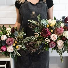 a woman holding two bouquets of flowers in front of her face and wearing an apron