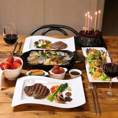 a wooden table topped with plates of food and glasses of wine