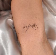 a small tattoo on the arm of a woman with mountains in the background and clouds above it