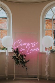 a pink neon sign that says,'crazy in love'next to balloons and flowers