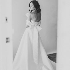 a woman in a long white dress is looking at her reflection while wearing a large bow