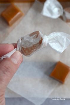 a hand holding a piece of food with wax paper on it and some pieces of cake in the background