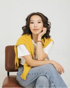 a woman sitting on top of a chair with her hand under her chin and looking at the camera