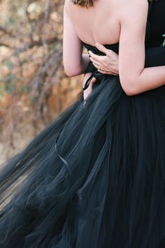 a woman in a black dress is holding her hand on her chest and looking at the camera