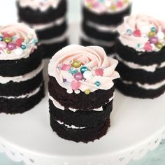 several chocolate cakes with frosting and sprinkles on a white cake plate