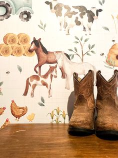 a pair of brown boots sitting on top of a wooden table next to a wall with farm animals