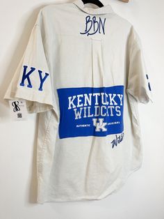 "One of a kind of Kentucky Wildcats shirt/jacket. This is a great gift for Kentucky fans. The shirt is upcycled (sanitized with Lysol laundry wash.) Custom upcycled T-shirt graphics are sewn on the back and vinyl Kentucky graphics are added all over the shirt.  Not one shirt is the same.  The shirt is great for any gender and can be styled as a shirt or jacket. It can be paired with a long sleeve shirt, flannel, t-shirt, or tank underneath. It can also be styled buttoned up or open. The model is Collegiate Cotton Collared Top, Collegiate Collared Cotton Top, Casual Cotton Shirt For Game Day, Relaxed Fit Cotton Shirt For Game Day, Casual Reworked Cotton Shirt, Shirt Flannel, Shirt Graphics, Washing Laundry, Kentucky Wildcats