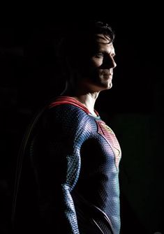 the man is wearing a superman costume and standing in the dark with his hands on his hips