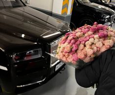 a man holding a large bouquet of flowers in front of a black car with other cars behind him