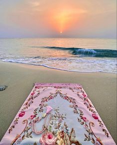 the sun is setting over the beach with a blanket on it and flowers in the foreground