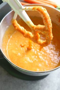 a whisk is being used to stir carrots in a saucepan on the stove