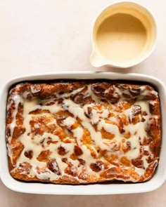 a casserole in a white dish with cream on top next to a cup of coffee