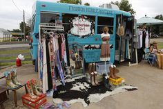 a blue bus parked in front of a store filled with clothes and boots on display