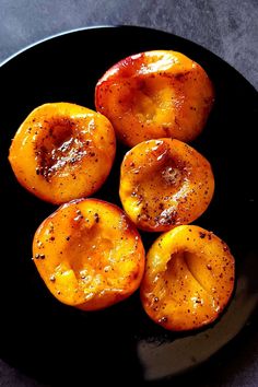 four pieces of cooked peaches on a black plate with seasoning sprinkles