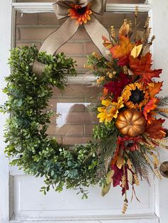 a wreath with autumn leaves and pumpkins hanging on the front door, next to a window