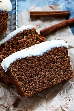 two slices of carrot cake with icing and cinnamon sticks next to them on top of parchment paper