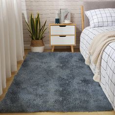 a bed room with a neatly made bed and a blue rug on the floor next to a window