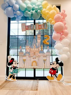 mickey and minnie mouse balloons in front of a large window with the castle on it