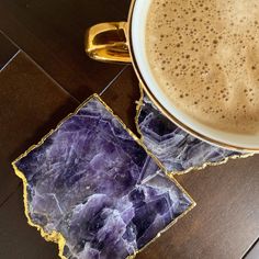 a cup of coffee sitting on top of a wooden table next to a purple coaster