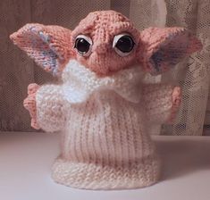 a knitted baby yoda doll with big eyes and a sweater on it's chest