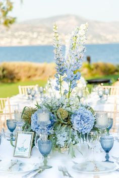 the table is set with blue and white flowers, silverware, and place settings