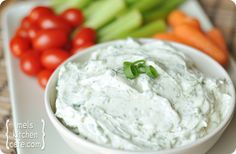 a white bowl filled with ranch dip surrounded by carrots, celery and tomatoes