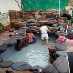 two men are playing in an outdoor pool with rocks and logs on the side walk