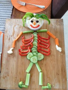 a wooden cutting board topped with cut up veggies and a clown face on top of it