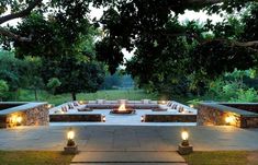 an outdoor fire pit surrounded by stone walls and benches with lit candles on each side