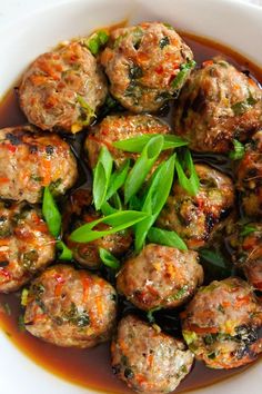 a white bowl filled with meatballs covered in sauce and garnished with green leaves