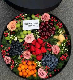 an arrangement of fruit and flowers is displayed in a black tray on the ground with a sign that reads snow floral design