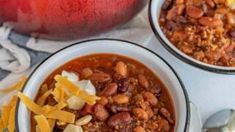 two bowls filled with chili and cheese next to an apple