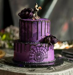 a purple wedding cake decorated with figurines and flowers on a table next to a cell phone