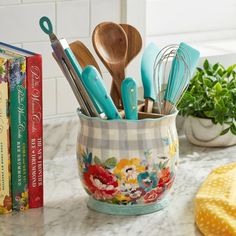 kitchen utensils and cookbooks are sitting in a flowered cup on the counter