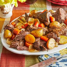 a white plate topped with meat and vegetables next to a vase filled with yellow flowers