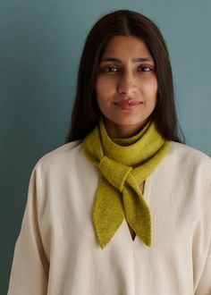 a woman wearing a white sweater and green scarf on her neck, standing in front of a blue wall