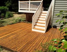 a wooden deck with steps leading up to a white railing on the side of a house