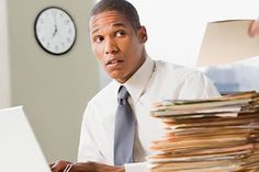 a man sitting in front of a laptop computer with stacks of papers on the desk