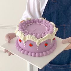 a person in overalls holding a cake with pink frosting and strawberries on it