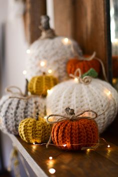 knitted pumpkins sitting on top of a wooden shelf with string lights around them